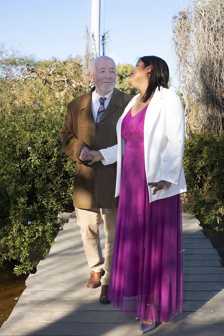 Un paso por detrás, Carlos contempla a Zoila con la ternura de quien ve en ella su horizonte. Ella gira suavemente el rostro, encontrando sus ojos como quien reconoce un refugio eterno. En ese cruce de miradas nace un lenguaje silencioso, una corriente de amor que los envuelve y los une.