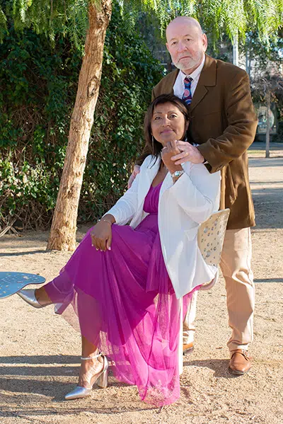 Carlos descansa sus manos sobre los hombros de Zoila, ofreciendo su apoyo en silencio. Ella, sentada en el parque, se siente segura, rodeada por el amor que se transmite a través de un simple gesto de cercanía.